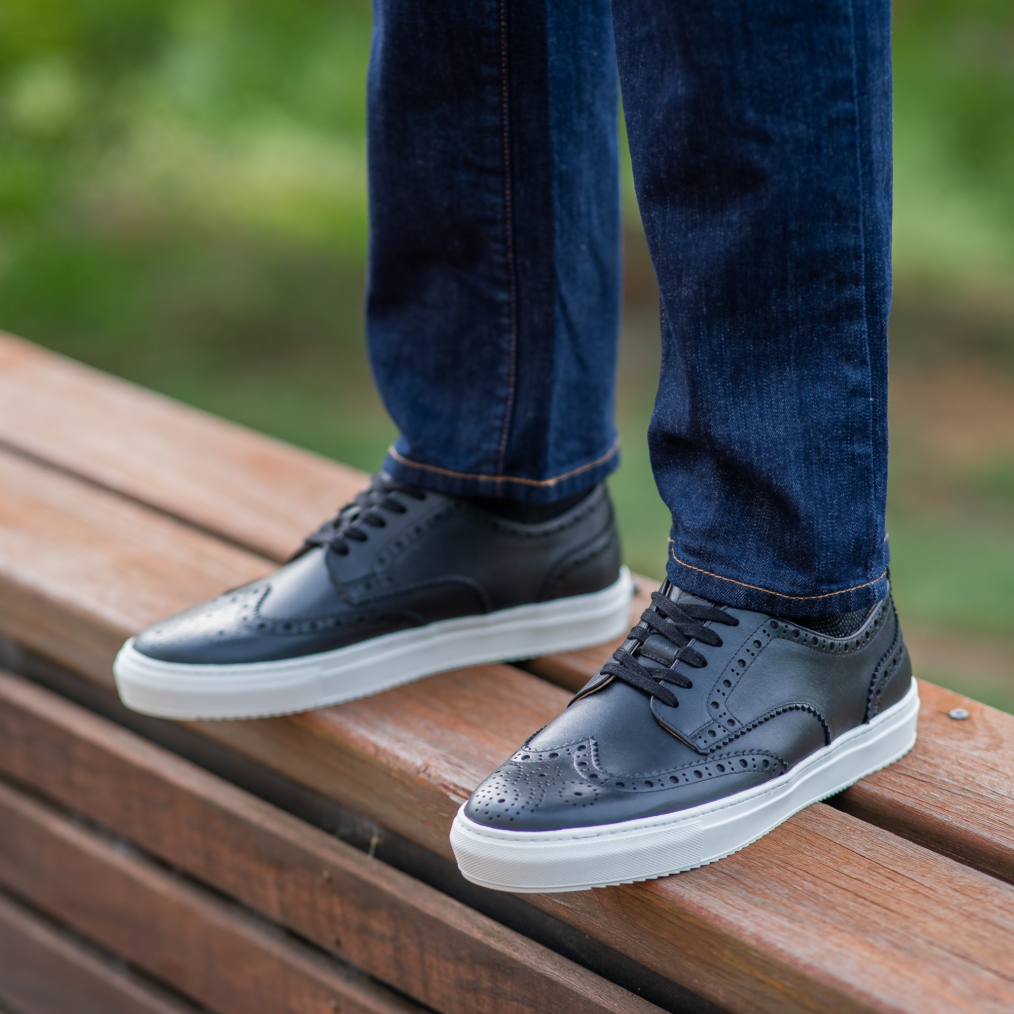 The Alpha low top wingtip sneakers in black with hand punches holes on the upper leather worn with blue jeans