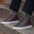 The Explorer men’s high top leather sneakers in brown, worn with black denim and grey striped casual shirt