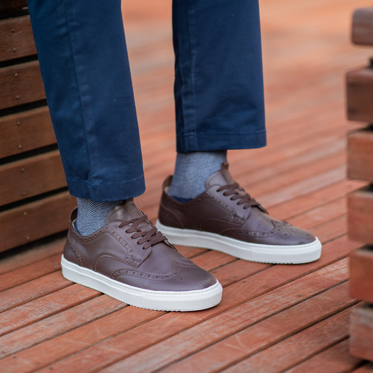 Mens low top brogue wingtip leather sneakers in espresso calfskin, paired with blue khaki and polo shirt