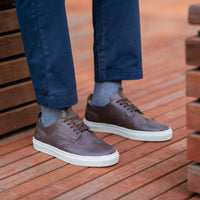 Mens low top brogue wingtip leather sneakers in espresso calfskin, paired with blue khaki and polo shirt