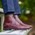 Burgundy brogue boots featuring wingtip design paired with blue jeans and printed cotton shirt