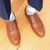 Mens tan brogues with wingtip design paired with dress pants and stripped shirt for professional look